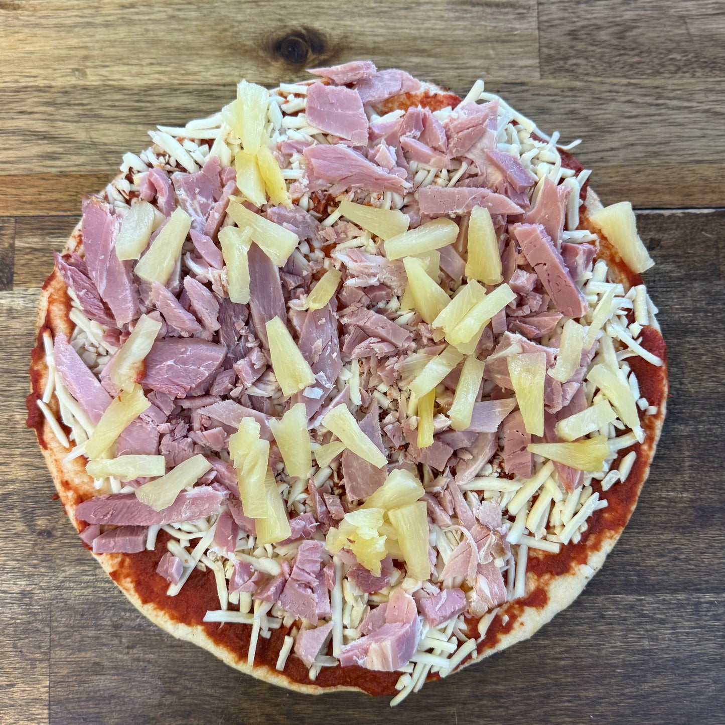 Ham and Pineapple Pizza topped with shredded ham and pineapple on a crust, ready for baking.