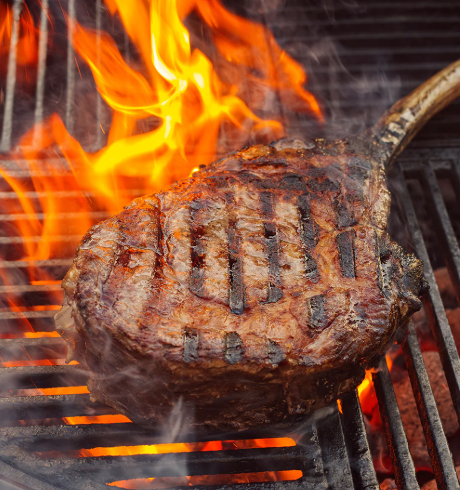Reverse-Seared Tomahawk Steak is being grilled over an open flame, showcasing its delicious grill marks.