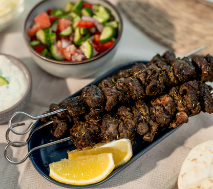 Lane's Herby Souvlaki Recipe Base skewers served with fresh salad and lemon slices on a blue plate.