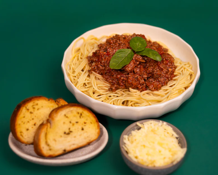 Lane's Nonna's Spaghetti Recipe Base served with garlic bread and grated cheese on a green background.