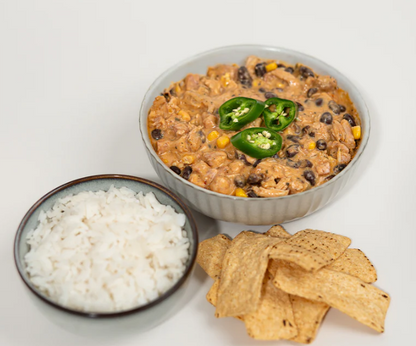 A bowl of Lane's Creamy White Chilli Recipe Base with rice and tortilla chips, garnished with jalapeños.