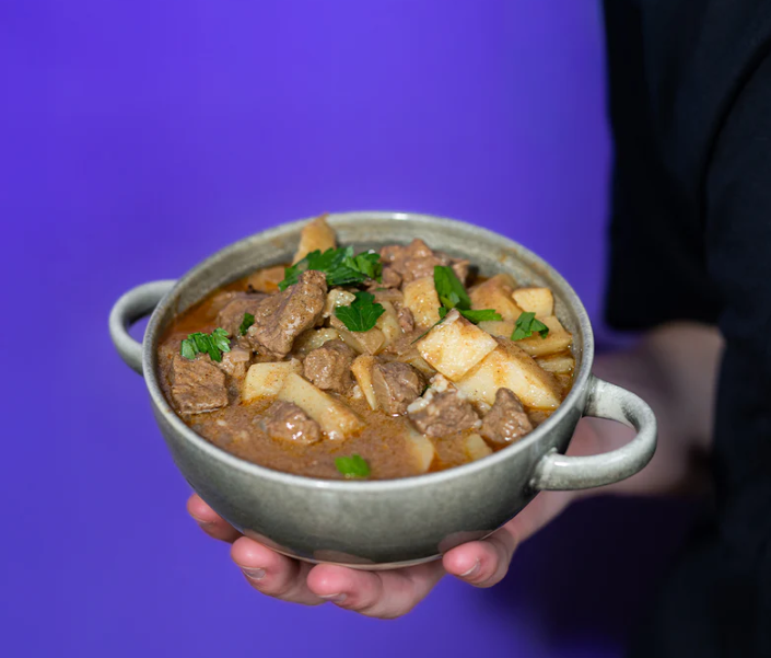 Bowl of Lane's Rich & Nutty Massaman Curry Recipe Base with beef and potatoes, garnished with fresh herbs.