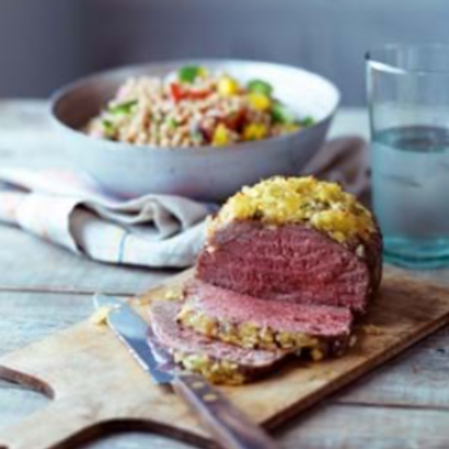 Moroccan Lamb Mini Roast 500g sliced on a wooden board next to a bowl of salad and a glass of water.